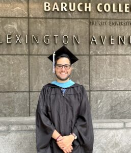 Brian Aguilar Avila in his MSEd cap and gown, standing in front of Baruch College